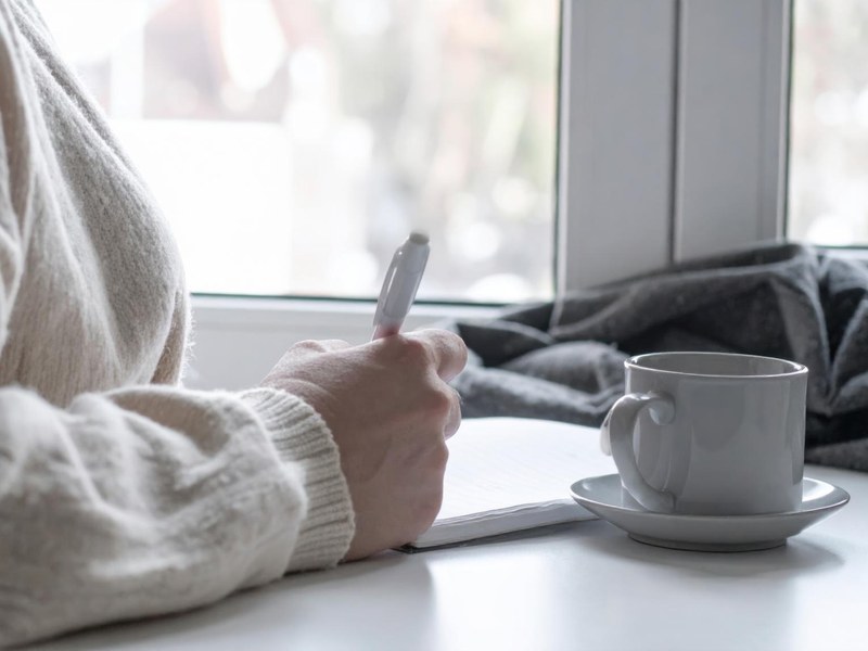 Pencere kenarında çay eşliğinde günlük yazan kadın